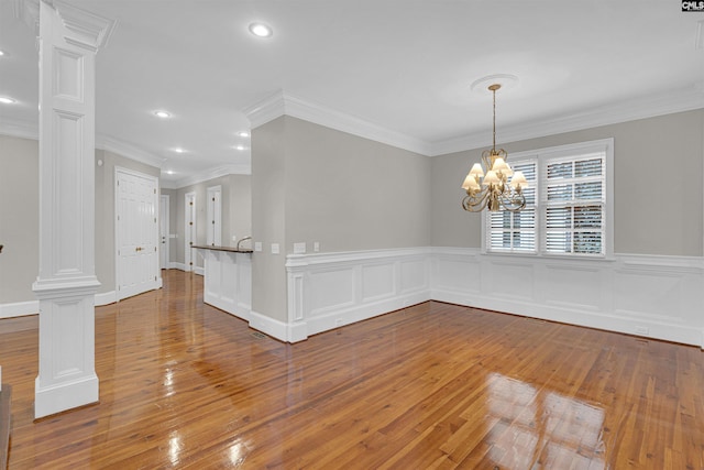 unfurnished room featuring decorative columns, ornamental molding, a chandelier, and hardwood / wood-style flooring