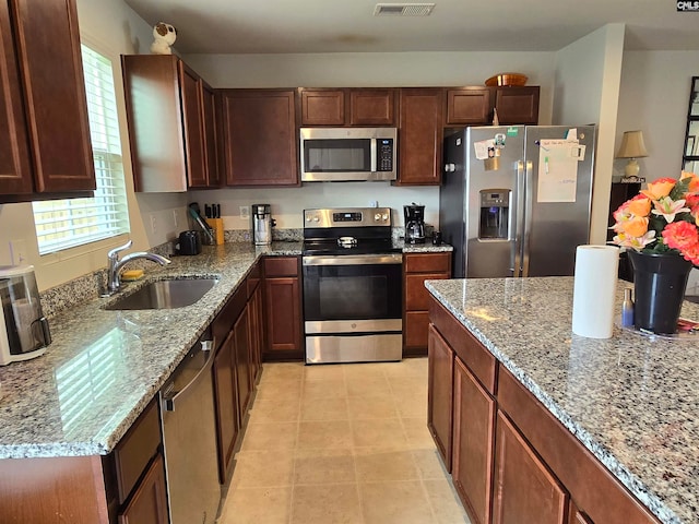 kitchen featuring appliances with stainless steel finishes, a healthy amount of sunlight, a sink, and light stone countertops