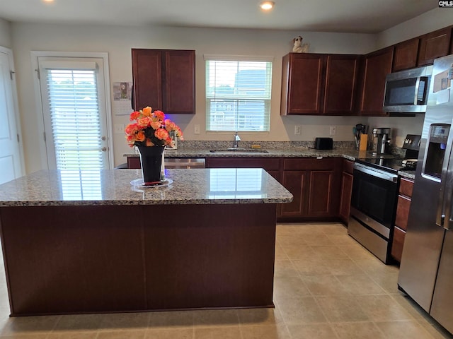 kitchen with a center island, stainless steel appliances, recessed lighting, a sink, and light stone countertops