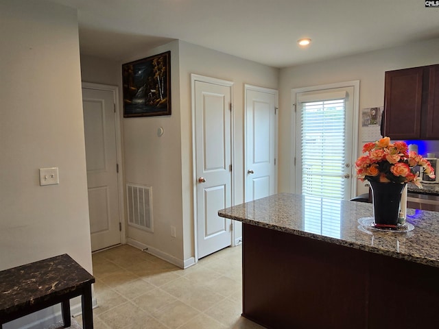 kitchen featuring visible vents, dark brown cabinets, light stone countertops, a peninsula, and baseboards