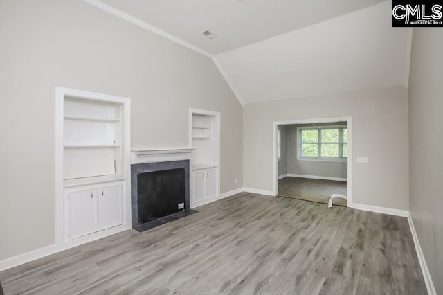 unfurnished living room with built in shelves, lofted ceiling, a tiled fireplace, and light wood-type flooring