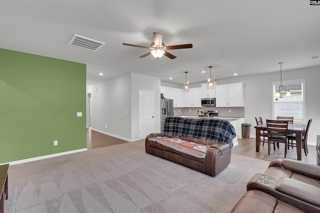 living room with ceiling fan with notable chandelier and light hardwood / wood-style flooring