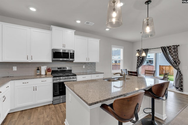 kitchen featuring light hardwood / wood-style floors, a kitchen island with sink, sink, hanging light fixtures, and appliances with stainless steel finishes