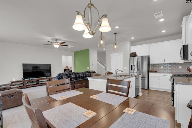 dining area with sink, ceiling fan with notable chandelier, and dark wood-type flooring