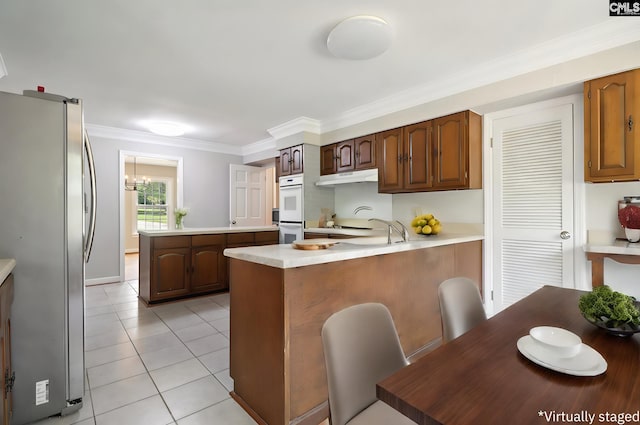 kitchen featuring light tile patterned flooring, kitchen peninsula, ornamental molding, double oven, and stainless steel fridge