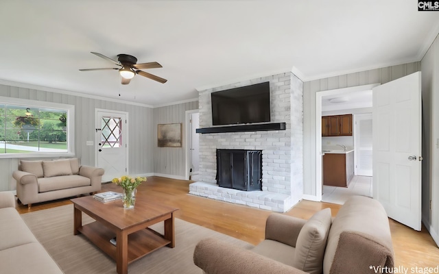 living room featuring ceiling fan, light hardwood / wood-style flooring, a brick fireplace, and crown molding