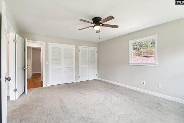 unfurnished bedroom with two closets, ceiling fan, and light colored carpet