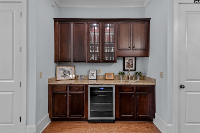 bar with dark brown cabinets, light hardwood / wood-style floors, beverage cooler, and sink