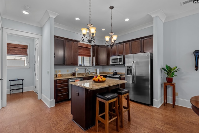 kitchen featuring light wood-type flooring, a center island, a notable chandelier, stainless steel appliances, and decorative light fixtures