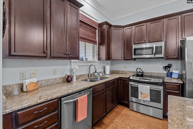 kitchen with appliances with stainless steel finishes, light stone countertops, light hardwood / wood-style flooring, dark brown cabinetry, and sink