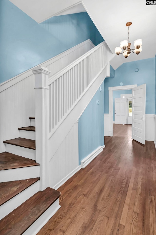 staircase with lofted ceiling, a chandelier, and hardwood / wood-style floors