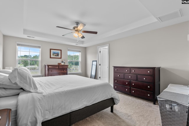 carpeted bedroom with ceiling fan, a raised ceiling, and multiple windows