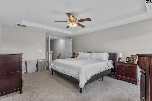 carpeted bedroom with a raised ceiling and ceiling fan