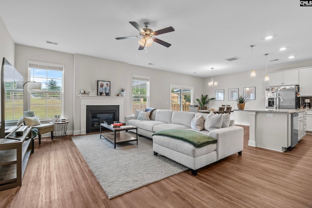 living room with ceiling fan with notable chandelier, a wealth of natural light, and light hardwood / wood-style floors