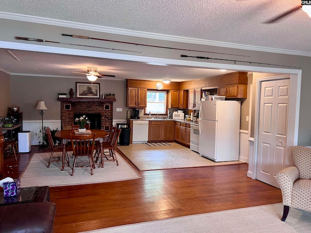 kitchen featuring light hardwood / wood-style floors, a brick fireplace, white appliances, a textured ceiling, and ceiling fan