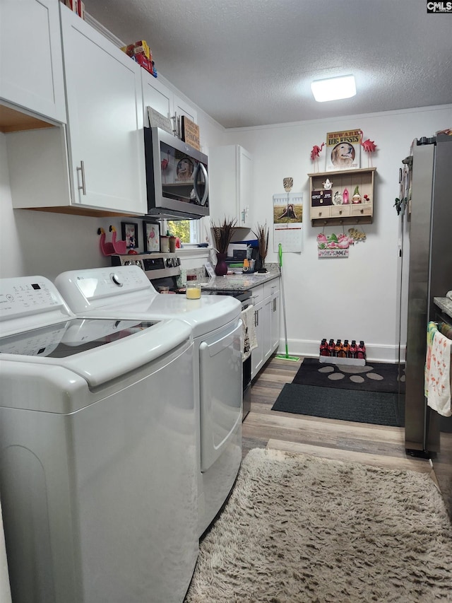 laundry room featuring light hardwood / wood-style flooring, washing machine and dryer, cabinets, and a textured ceiling