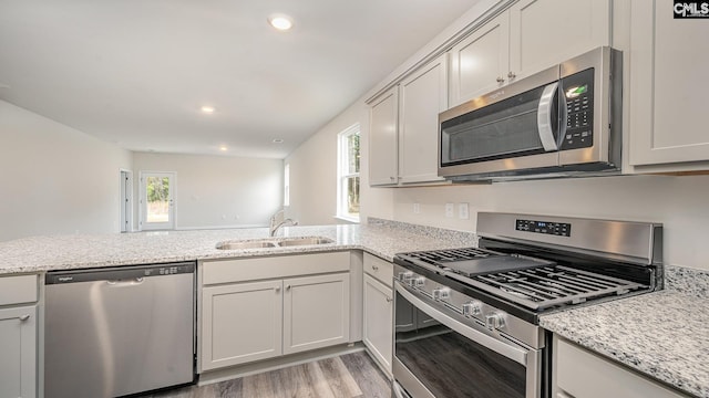 kitchen featuring kitchen peninsula, appliances with stainless steel finishes, light stone countertops, sink, and light hardwood / wood-style floors