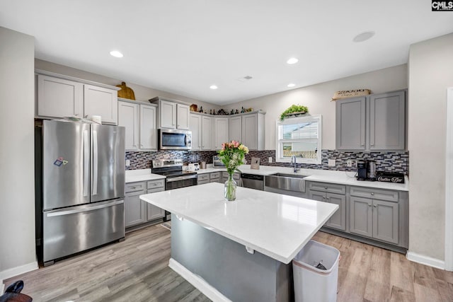 kitchen with sink, a kitchen island, light hardwood / wood-style flooring, gray cabinetry, and appliances with stainless steel finishes