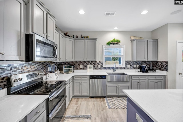 kitchen with appliances with stainless steel finishes, sink, tasteful backsplash, and light hardwood / wood-style flooring