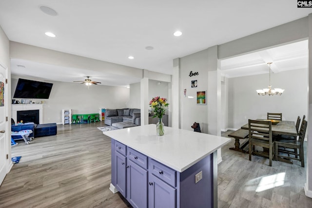 kitchen with ceiling fan with notable chandelier, pendant lighting, a center island, and light hardwood / wood-style flooring