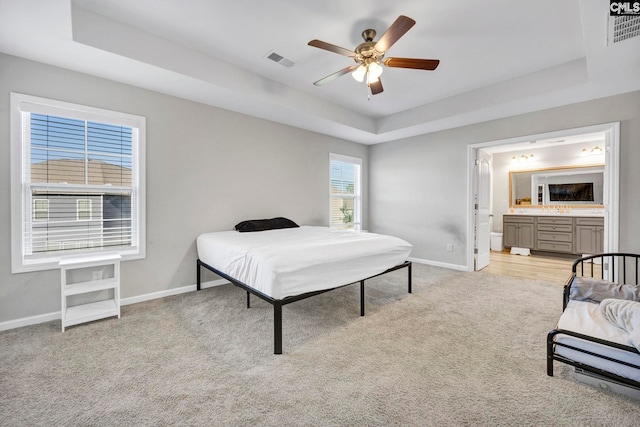 bedroom with light carpet, a tray ceiling, ceiling fan, and ensuite bathroom