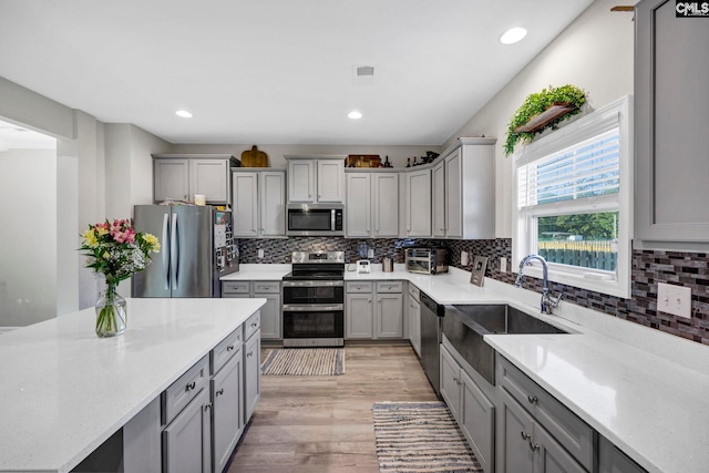 kitchen featuring decorative backsplash, light hardwood / wood-style floors, gray cabinets, stainless steel appliances, and sink