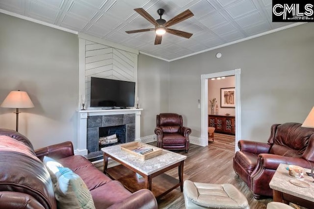 living room with ceiling fan, hardwood / wood-style flooring, a tiled fireplace, and crown molding