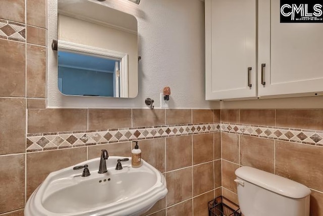 bathroom with toilet, tile walls, and sink