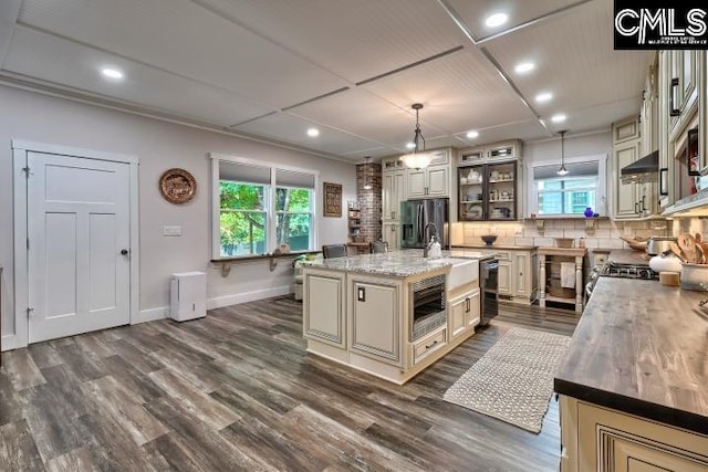 kitchen with light stone counters, an island with sink, decorative light fixtures, stainless steel appliances, and dark hardwood / wood-style floors