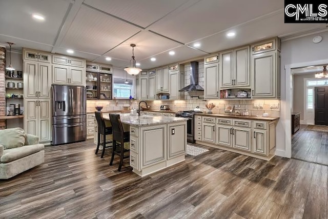 kitchen featuring hanging light fixtures, a kitchen island with sink, wall chimney exhaust hood, stainless steel appliances, and dark hardwood / wood-style flooring