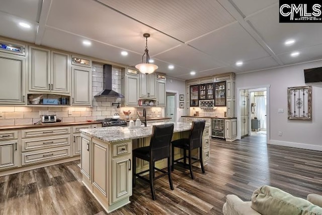 kitchen with dark wood-type flooring, a breakfast bar, a kitchen island, pendant lighting, and wall chimney range hood