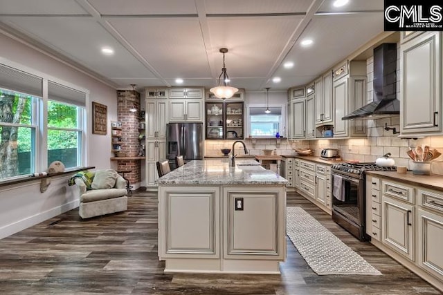 kitchen featuring pendant lighting, an island with sink, wall chimney exhaust hood, stainless steel appliances, and dark hardwood / wood-style floors