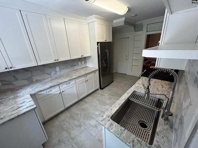 kitchen featuring light stone countertops, refrigerator with ice dispenser, white cabinets, and backsplash