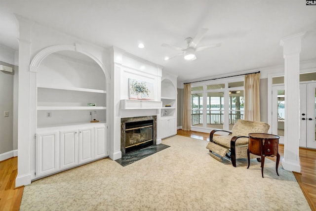 living room with light hardwood / wood-style flooring, a high end fireplace, ceiling fan, and built in features