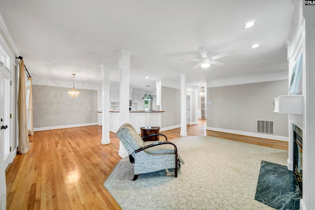 living room featuring ceiling fan with notable chandelier, wood-type flooring, and ornate columns