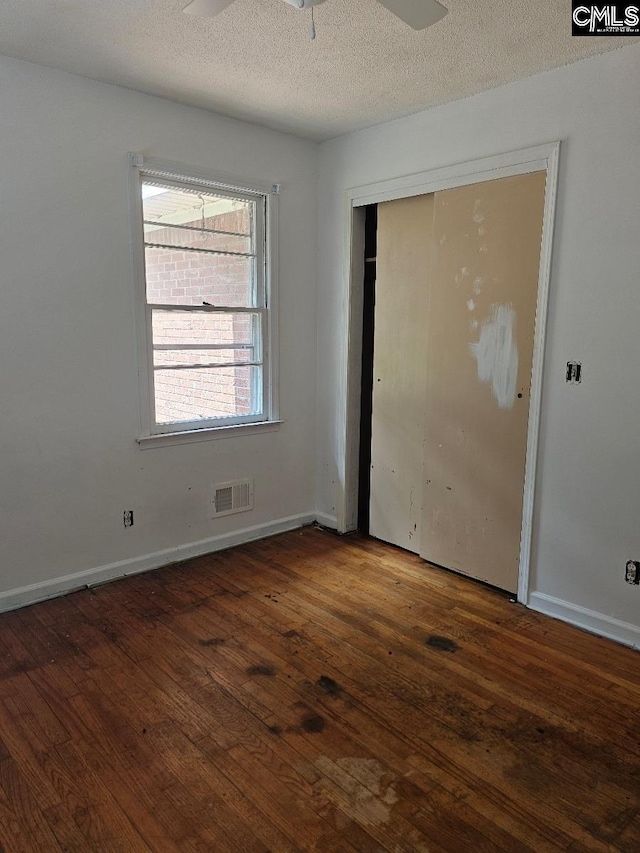 unfurnished bedroom featuring a closet, ceiling fan, dark hardwood / wood-style floors, and a textured ceiling