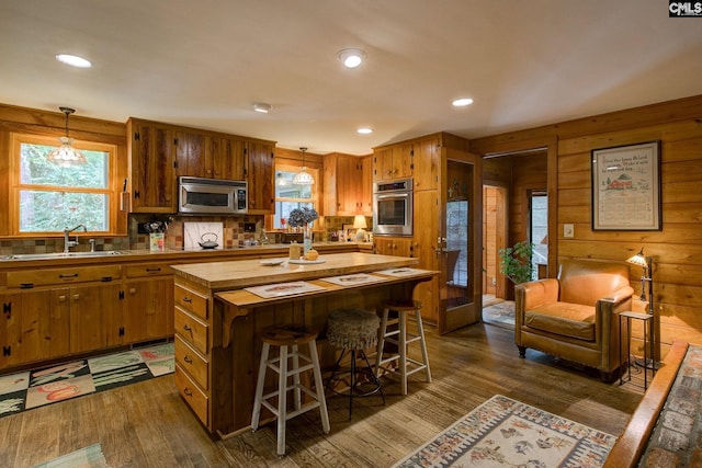 kitchen featuring pendant lighting, dark hardwood / wood-style floors, sink, stainless steel appliances, and wooden walls