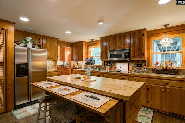 kitchen with hanging light fixtures, dark hardwood / wood-style floors, stainless steel appliances, and tasteful backsplash