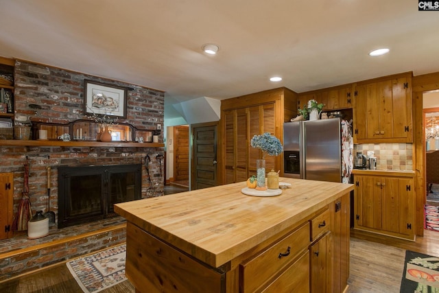 kitchen with decorative backsplash, a fireplace, a kitchen island, hardwood / wood-style flooring, and stainless steel fridge with ice dispenser