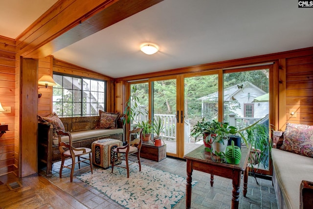 living room with a wealth of natural light, lofted ceiling, and wooden walls