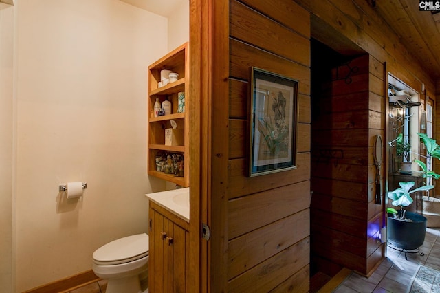 bathroom with wooden walls, toilet, and vanity