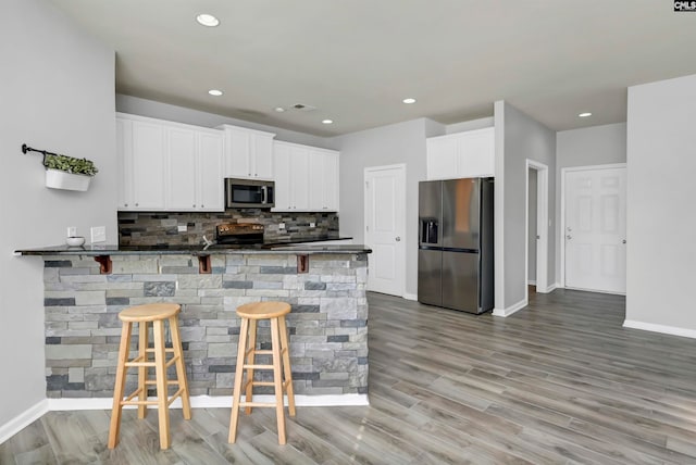 kitchen featuring kitchen peninsula, white cabinetry, appliances with stainless steel finishes, a kitchen breakfast bar, and light hardwood / wood-style floors