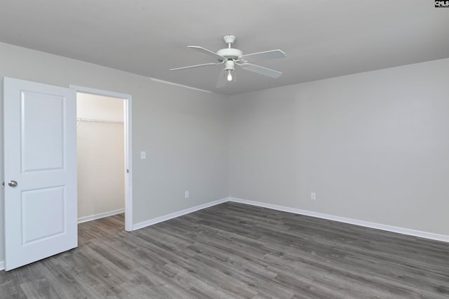 unfurnished bedroom featuring a closet, ceiling fan, a walk in closet, and dark hardwood / wood-style flooring