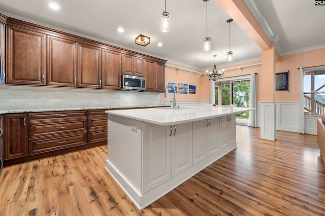 kitchen with an island with sink, light hardwood / wood-style floors, ornamental molding, a kitchen bar, and decorative light fixtures