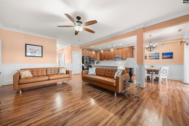 living room with ceiling fan with notable chandelier, light wood-type flooring, and crown molding