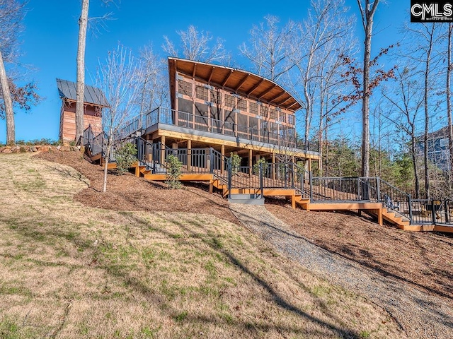 back of house with a sunroom, a deck, and a lawn