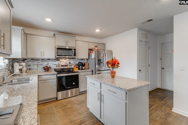 kitchen featuring light wood-type flooring, a center island, sink, stainless steel appliances, and light stone countertops