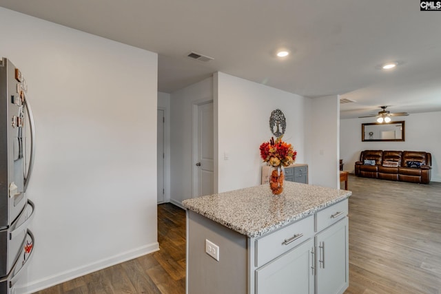 kitchen featuring light stone counters, a center island, dark hardwood / wood-style floors, stainless steel refrigerator, and ceiling fan