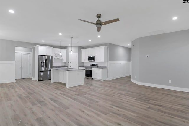 kitchen featuring white cabinets, pendant lighting, a kitchen island with sink, stainless steel appliances, and light wood-type flooring