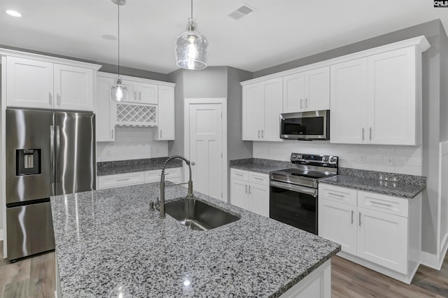 kitchen with hanging light fixtures, stainless steel appliances, wood-type flooring, a kitchen island with sink, and sink